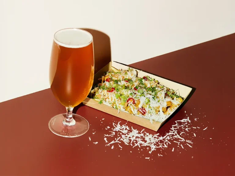 Tallrik med pasta toppad med riven ost och örter bredvid ett glas öl